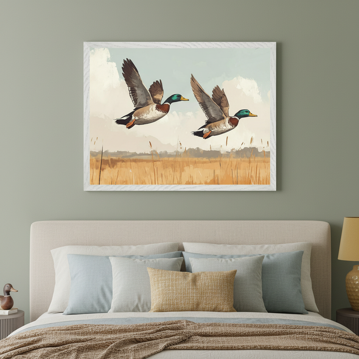 Modern bedroom with a beige upholstered bed and sage green wall. A framed print of two mallard ducks flying over a marsh in a painterly style hangs centered above the bed.