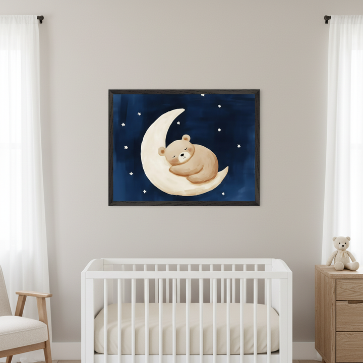 Modern nursery with a white crib and a wooden armchair. A large framed print of a cute brown bear sleeping on a crescent moon with white stars on a dark blue background hangs centered above the crib. A wooden dresser with a teddy bear sits to the right.