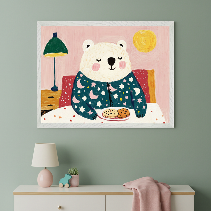 Kid's room with a white dresser against a sage green wall. A framed painting of a smiling white bear in pajamas eating cookies in bed, in an illustrative style, hangs above the dresser.