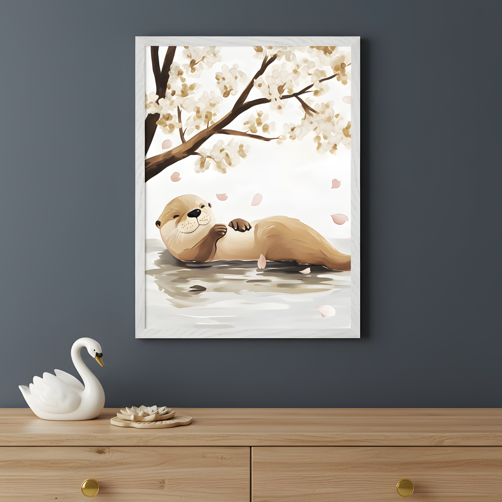 Framed wall art of a relaxed otter floating on its back in calm water, gazing up with a gentle smile as pink flower petals drift down from a blossoming tree above. The background features soft white and beige tones, creating a peaceful, springtime feel. A ceramic swan and a lotus-shaped dish sit on the wooden dresser beneath, enhancing the tranquil scene.
