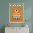 Kid's room with a blue-green wall. A framed poster with 'LET'S READ' and a cartoon brown bear holding books saying 'BE KIND', 'YOU ARE LOVED', 'YOU GOT THIS', 'DREAM BIG' hangs centered above a white and wood dresser. A teddy bear sits on the dresser.