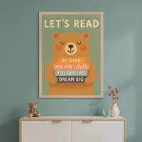 Kid's room with a blue-green wall. A framed poster with 'LET'S READ' and a cartoon brown bear holding books saying 'BE KIND', 'YOU ARE LOVED', 'YOU GOT THIS', 'DREAM BIG' hangs centered above a white and wood dresser. A teddy bear sits on the dresser.