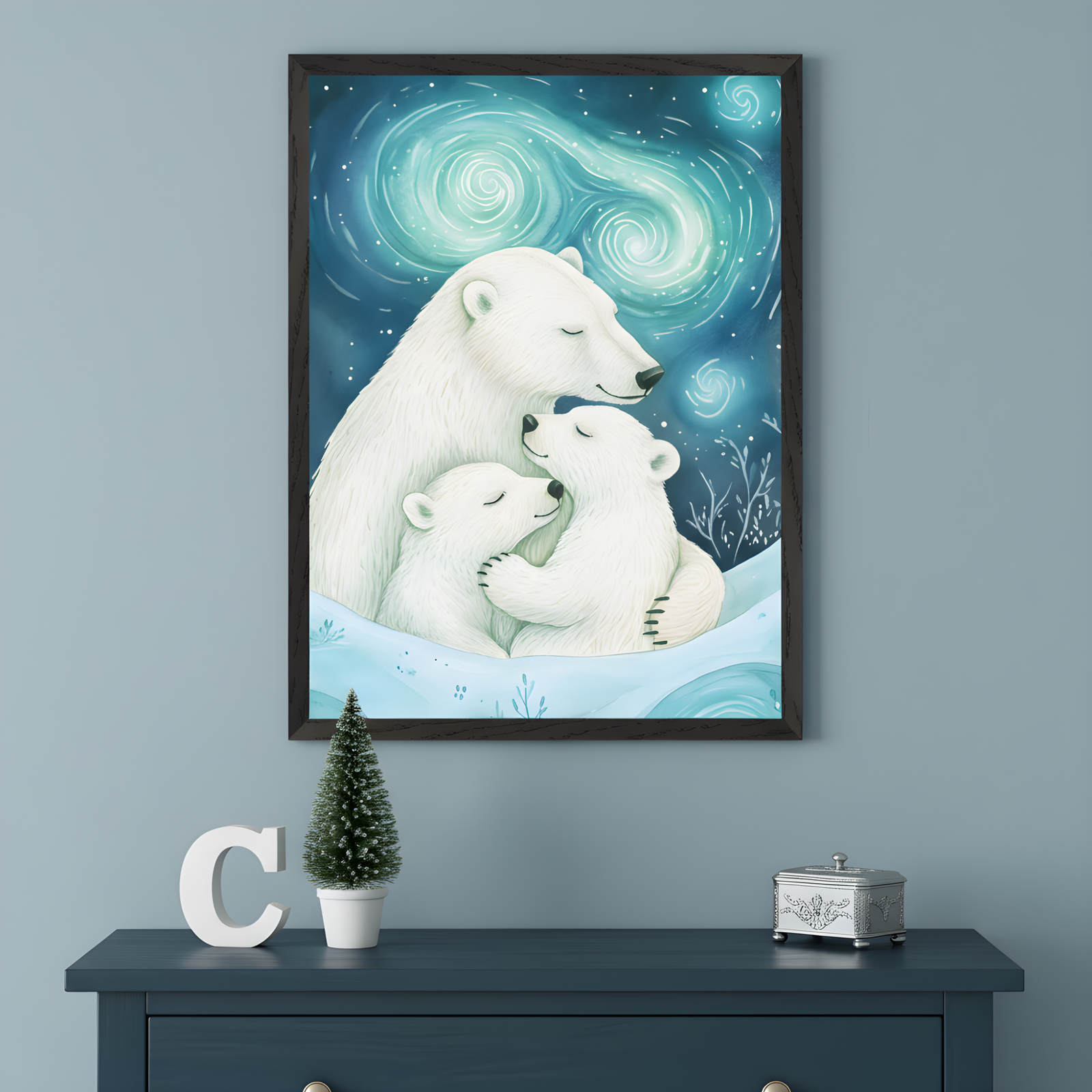 A framed illustration of a polar bear cuddling two cubs in a snowy landscape under a swirling, glowing aurora borealis sky. The artwork hangs above a dark blue dresser decorated with a small potted Christmas tree, a white letter "C," and a silver trinket box, creating a cozy winter vibe.