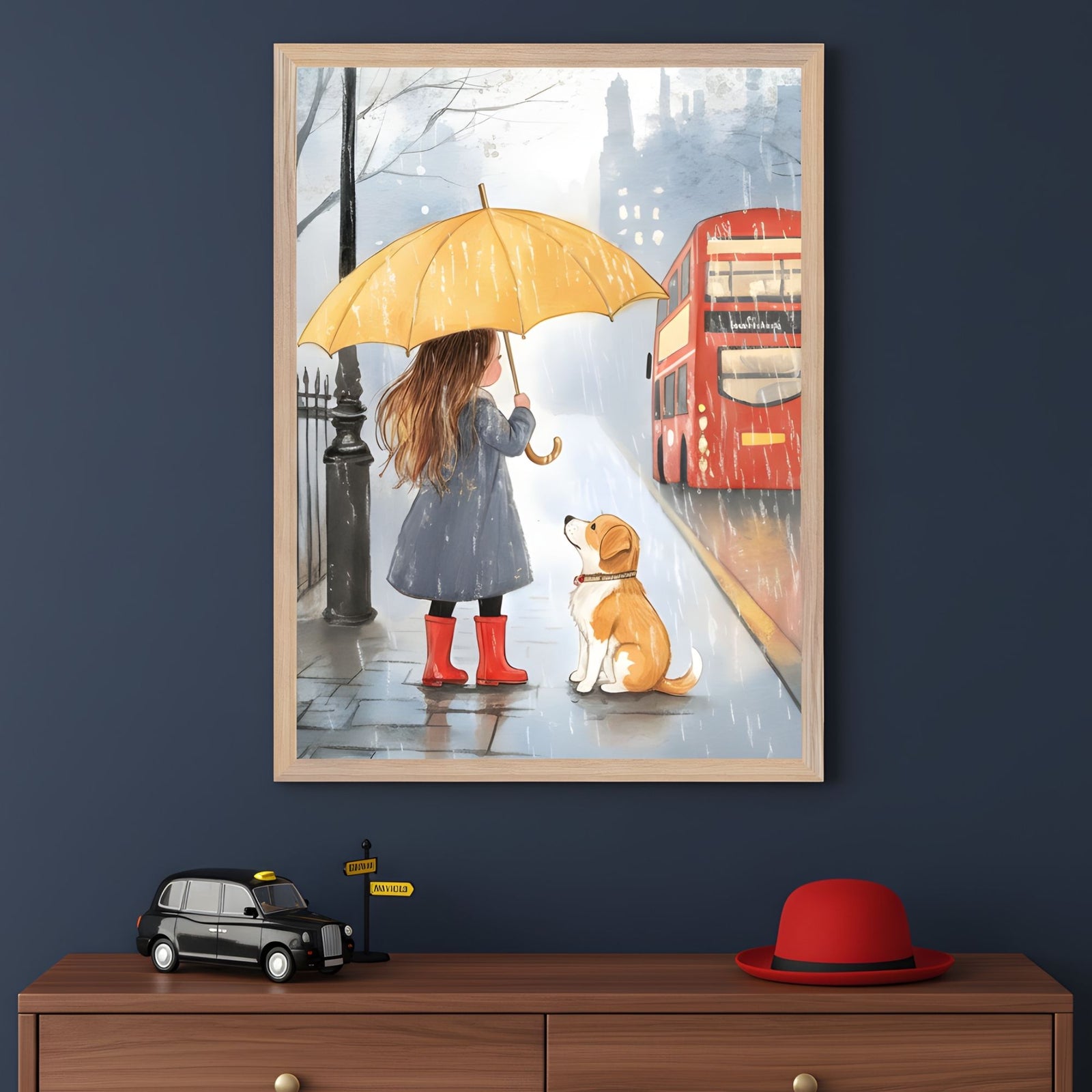 A framed illustration of a young girl in a navy coat and red rain boots holding a yellow umbrella while standing beside a dog in the rain, watching a red double-decker bus drive by. The scene evokes a rainy day in London and is displayed above a dresser with a toy black cab, a yellow street sign, and a red bowler hat.