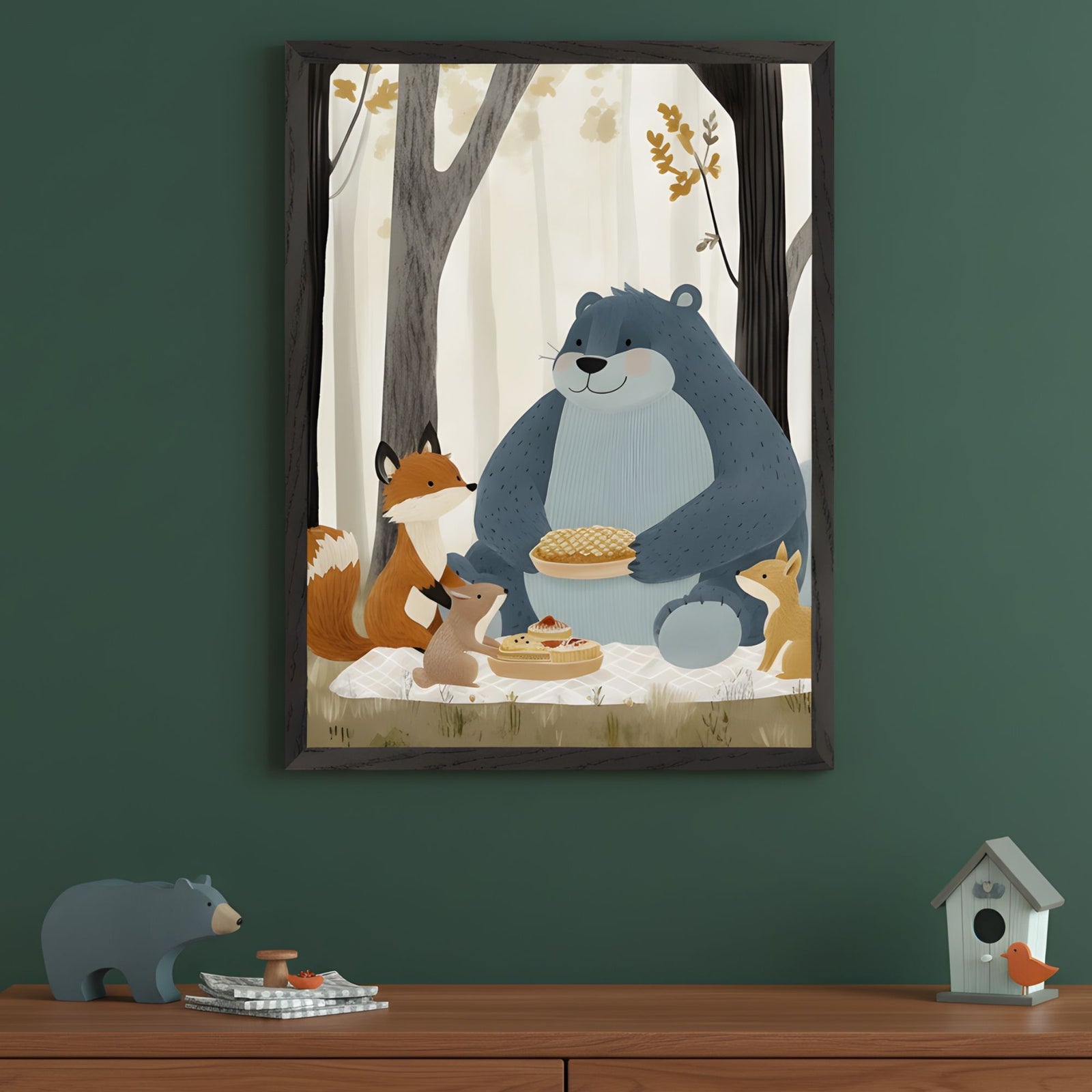Framed wall art featuring an illustrated forest picnic with a smiling blue bear holding a pie, surrounded by a fox, two rabbits, and a squirrel. The animals sit on a checkered blanket in a softly lit forest, with another pie and a stack of pancakes in front of them. The decor below includes a bear figurine, tiny mushrooms, and a birdhouse with an orange bird, complementing the cozy woodland theme.