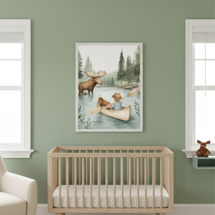 Modern nursery with a wood crib. A framed watercolor of a child in a canoe meeting a moose on a lake with pine trees, hangs centered above the crib on a green wall. A cream armchair and a shelf with a toy moose are visible.