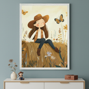 White-framed illustration of a smiling girl in a brown hat and vest, sitting on a hay bale in a field with butterflies and wildflowers. It hangs centered above a white dresser in a modern room.