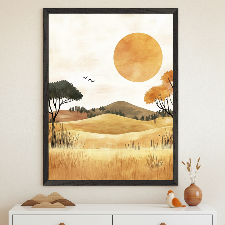 Framed wall art depicting a golden countryside scene with rolling hills, tall grasses, and scattered trees in warm autumn tones. A large orange sun dominates the sky as two birds fly nearby, creating a serene and dreamy atmosphere.