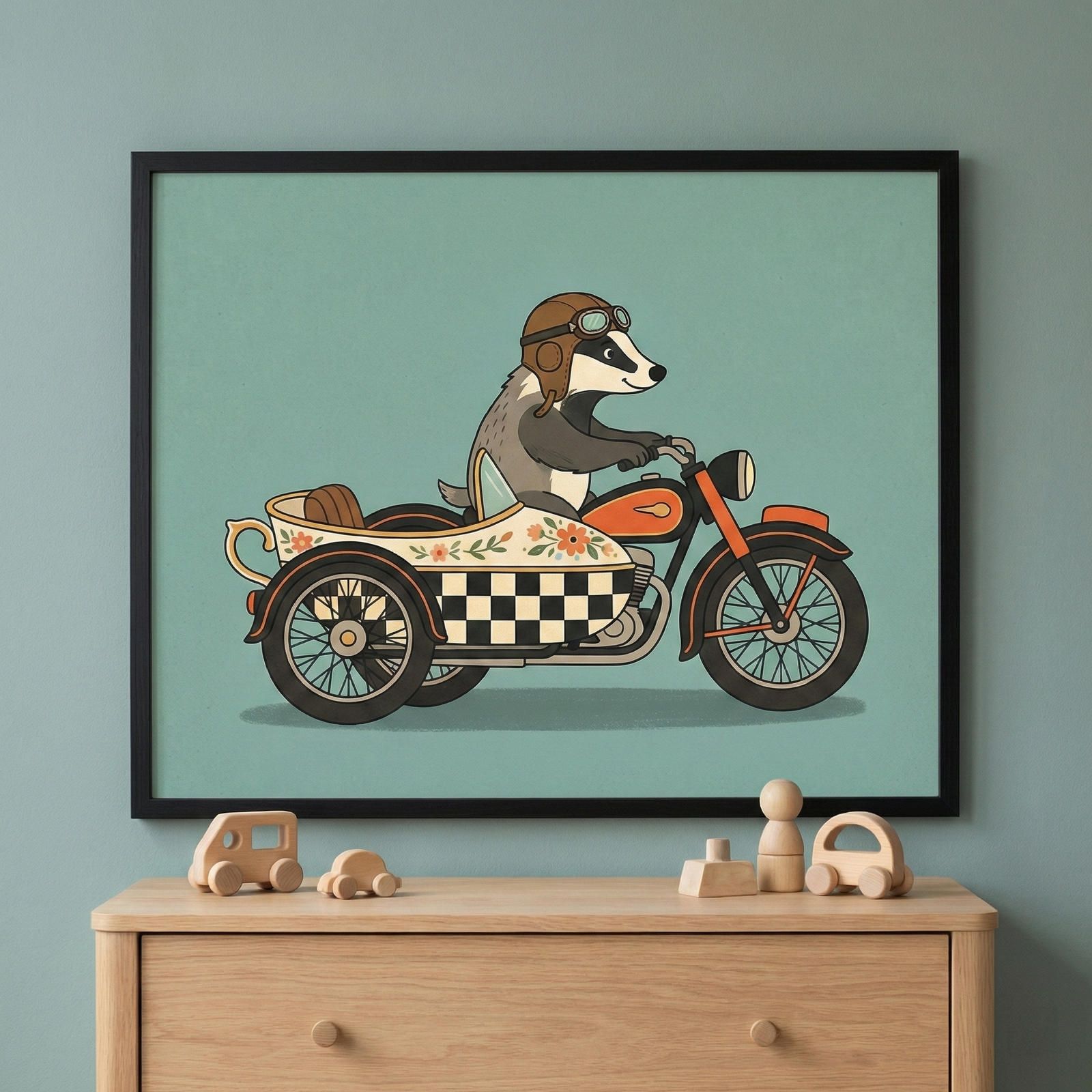 Framed badger on a motorcycle with a sidecar wall art in a black frame, mounted on a muted teal wall above a light wood dresser featuring several small wooden toys.