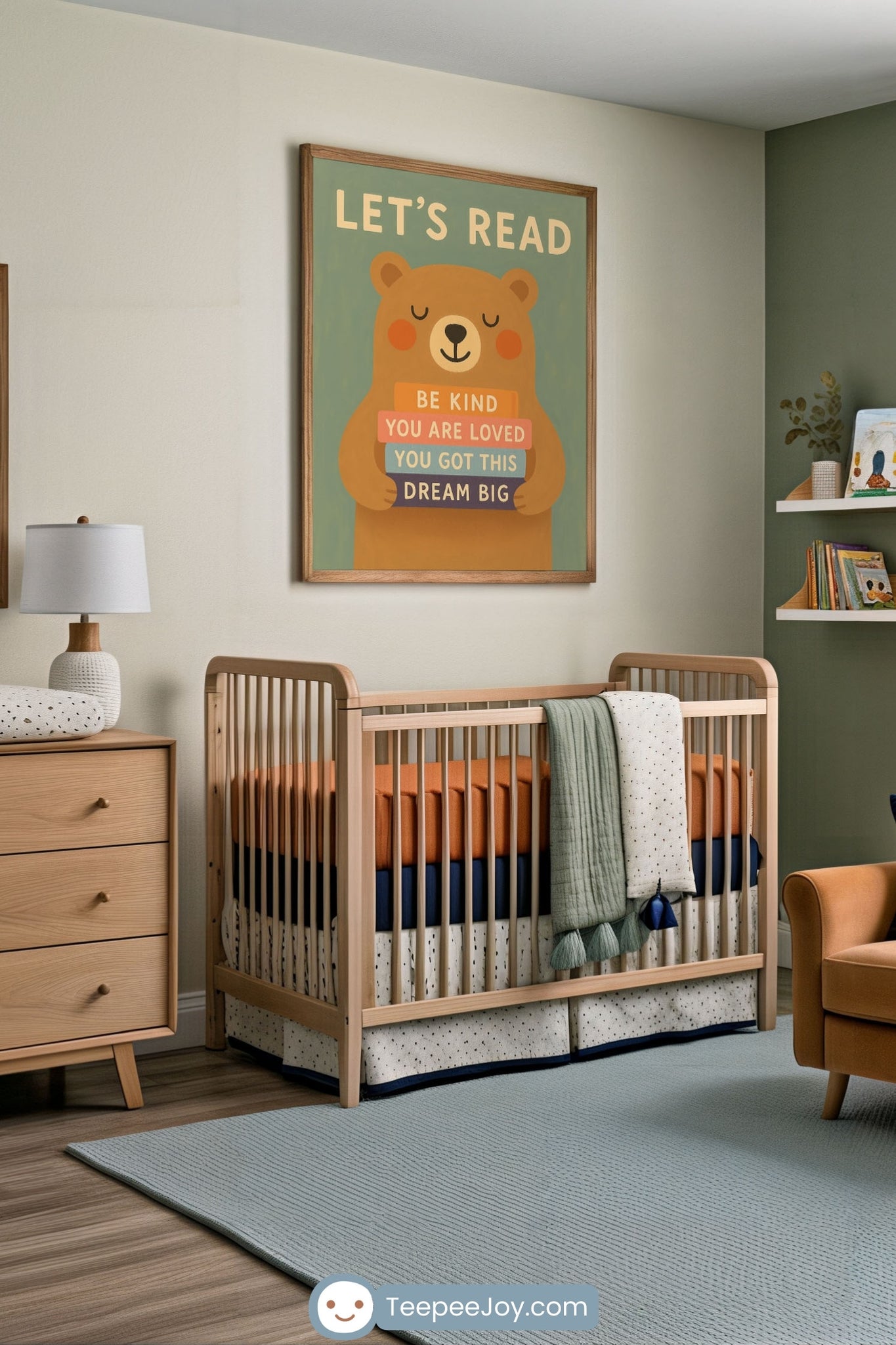 Cozy nursery with a wood crib featuring orange, navy, and polka-dot bedding, under a framed wall art of a smiling bear holding colorful books that read: “Be Kind,” “You Are Loved,” “You Got This,” and “Dream Big,” with the heading “Let’s Read.” The room includes soft green and wood tones, a dresser with a lamp, and shelves with children’s books and toys.