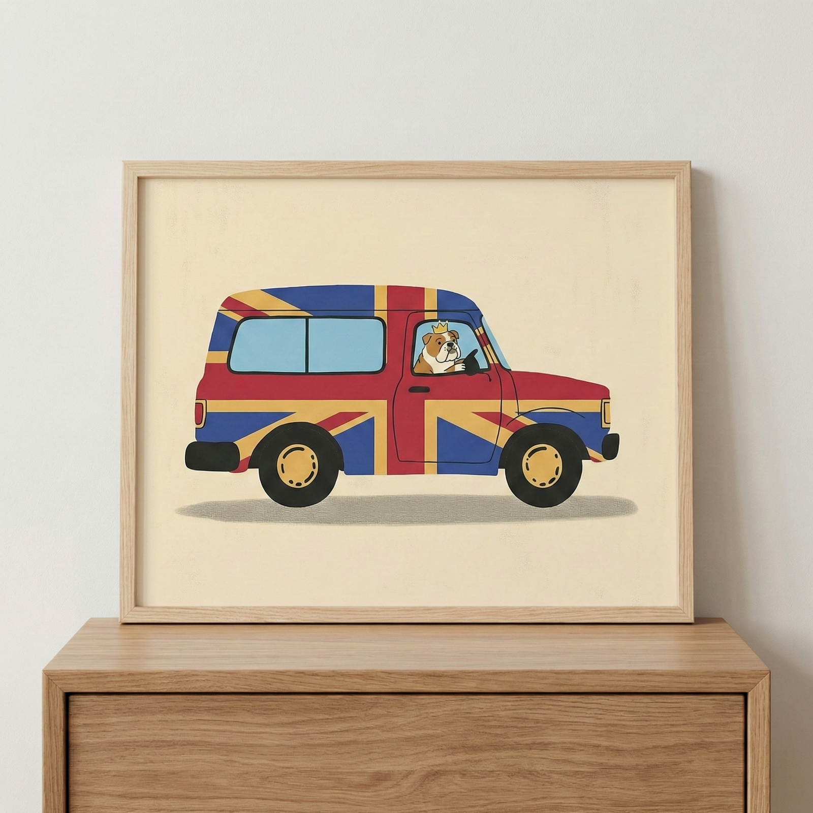 Framed bulldog driving a British flag car wall art sitting on a wooden chest of drawers against a white wall.