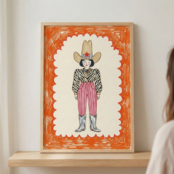 Framed crayon-style drawing of a fashionable cowboy figure with a zebra-striped shirt, high-waisted pink pants, silver boots, and a large tan hat with a red star. The bold orange scalloped border adds a playful, energetic touch to the portrait.