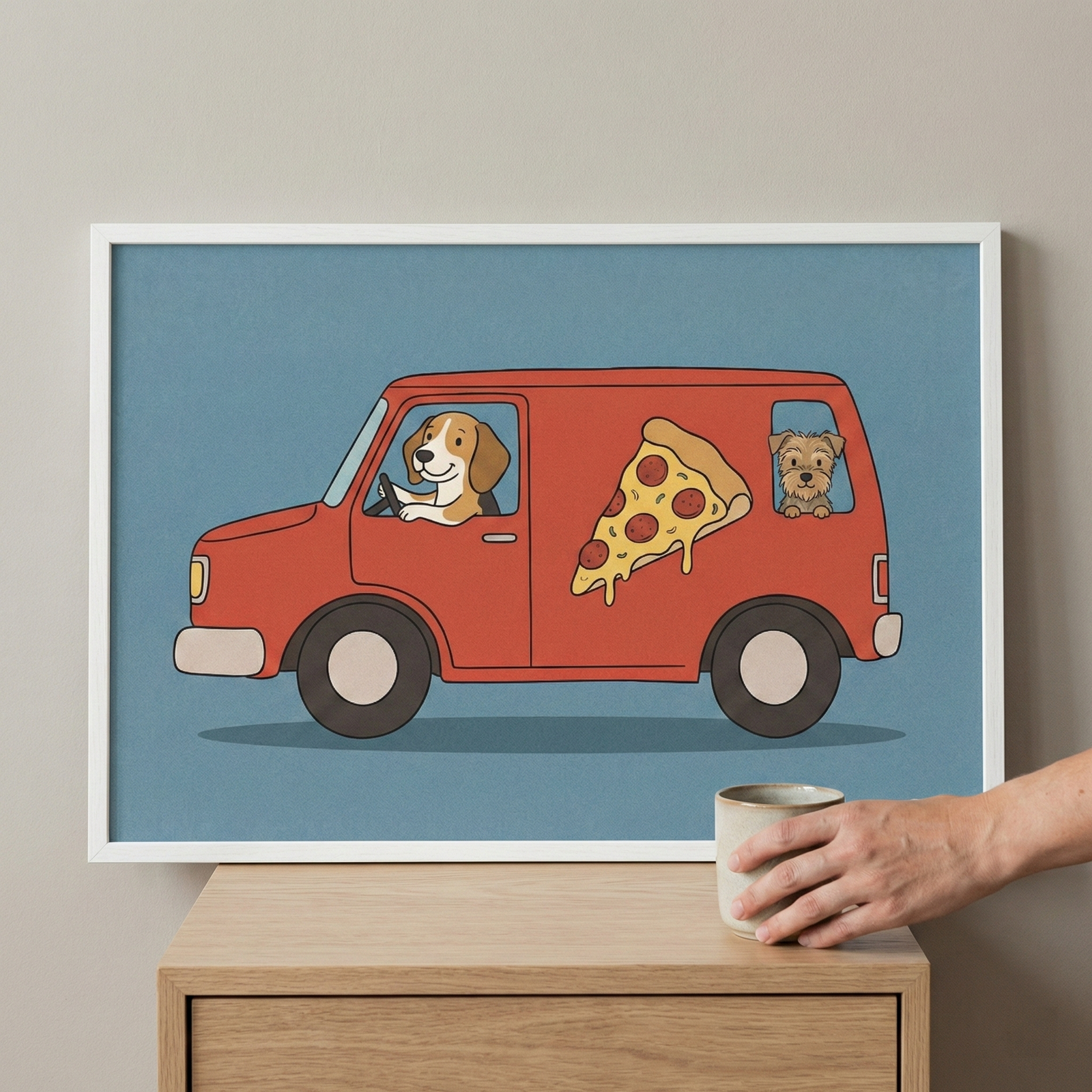 Framed wall art featuring a cute dog driving a red van with a pizza graphic, displayed in a white frame on a wooden surface next to a hand holding a ceramic mug.