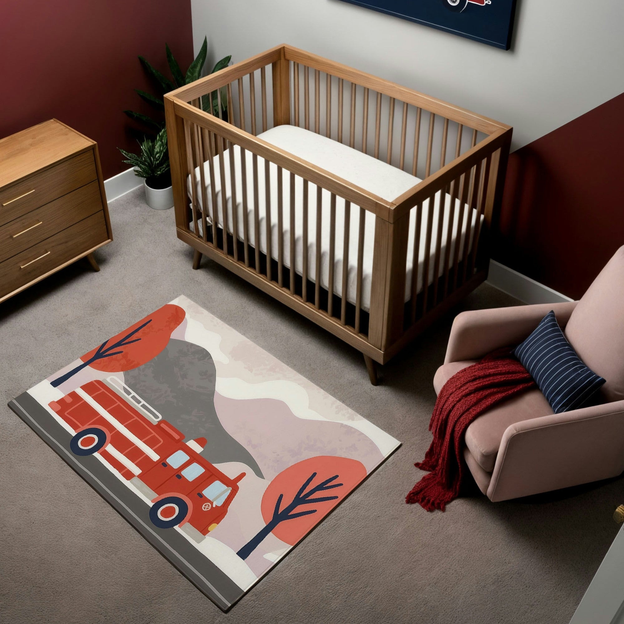 A modern nursery featuring a natural wood crib and dresser, set against a warm color palette with a maroon and white accent wall. The room includes a soft pink armchair with a striped navy pillow and a red knit blanket. A whimsical area rug depicts a bright red fire truck driving past stylized trees in autumnal tones, adding a playful and cozy touch to the space.