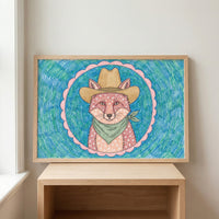 Framed western cowboy fox wall art in a light wood frame resting on a matching wooden shelf against a white wall.