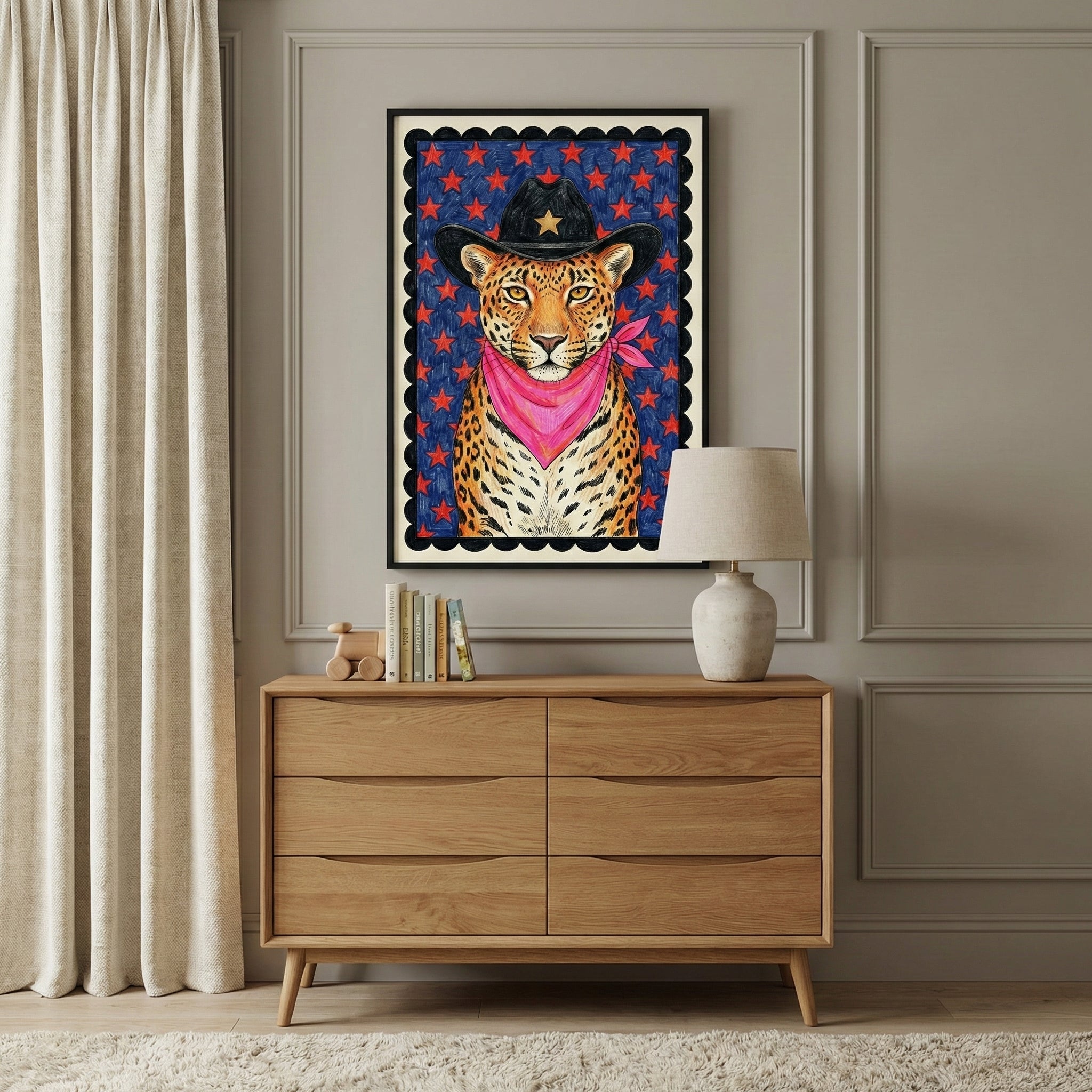 A framed illustration of a leopard wearing a black cowboy hat with a gold star and a bright pink bandana hangs above a modern wooden dresser. The room features elegant wall molding, neutral curtains, and a soft white rug.