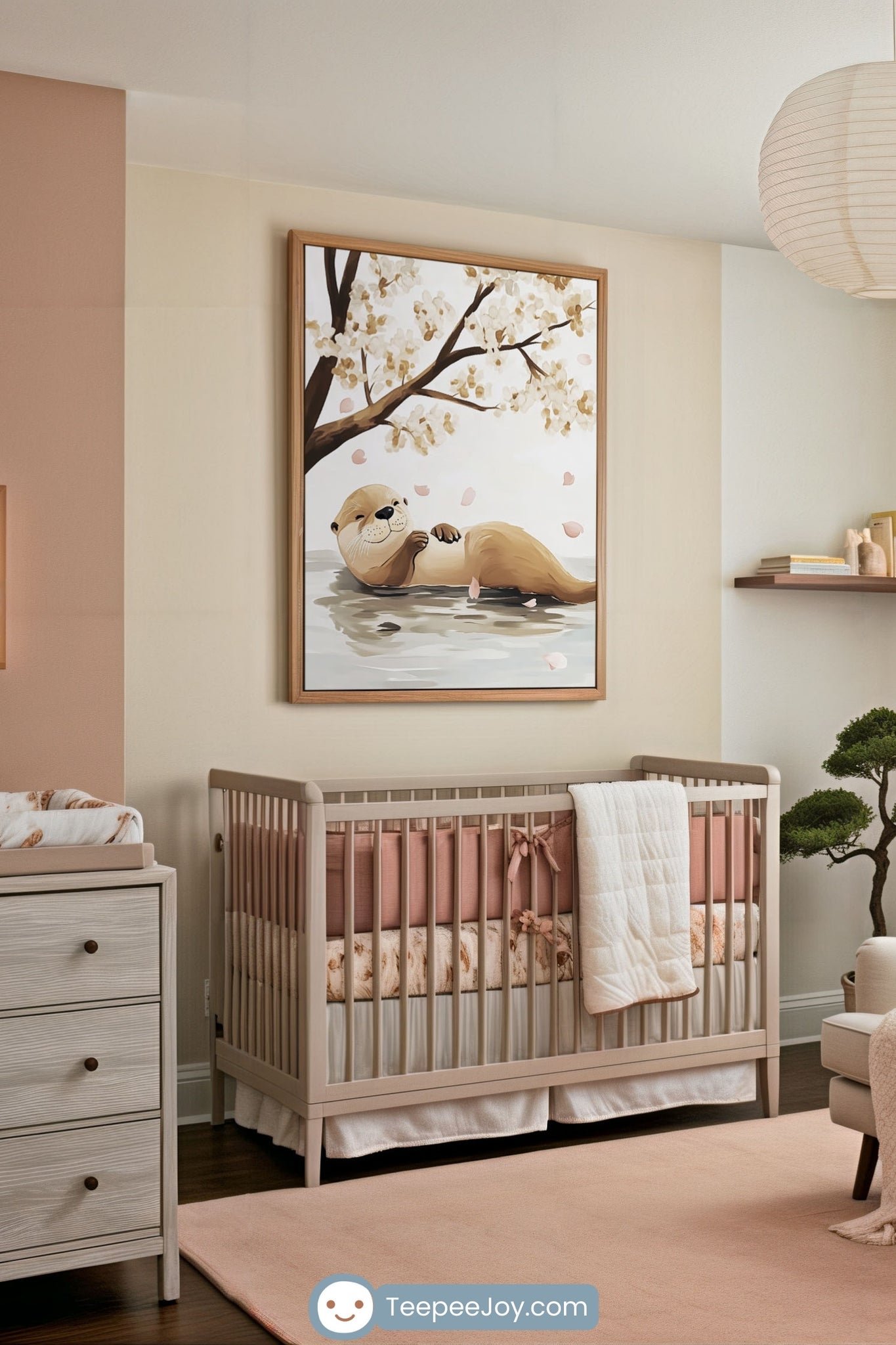 Stylish nursery room featuring a neutral-toned crib with soft pink and cream bedding, set beneath a large framed wall art of a smiling otter floating on water with cherry blossom petals falling around. The space is accented with a bonsai tree, floating shelves, and a warm, minimalist aesthetic.