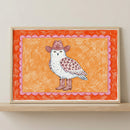 Framed cowboy owl animal wall art in a light wood frame sitting on a wooden shelf against a neutral wall.