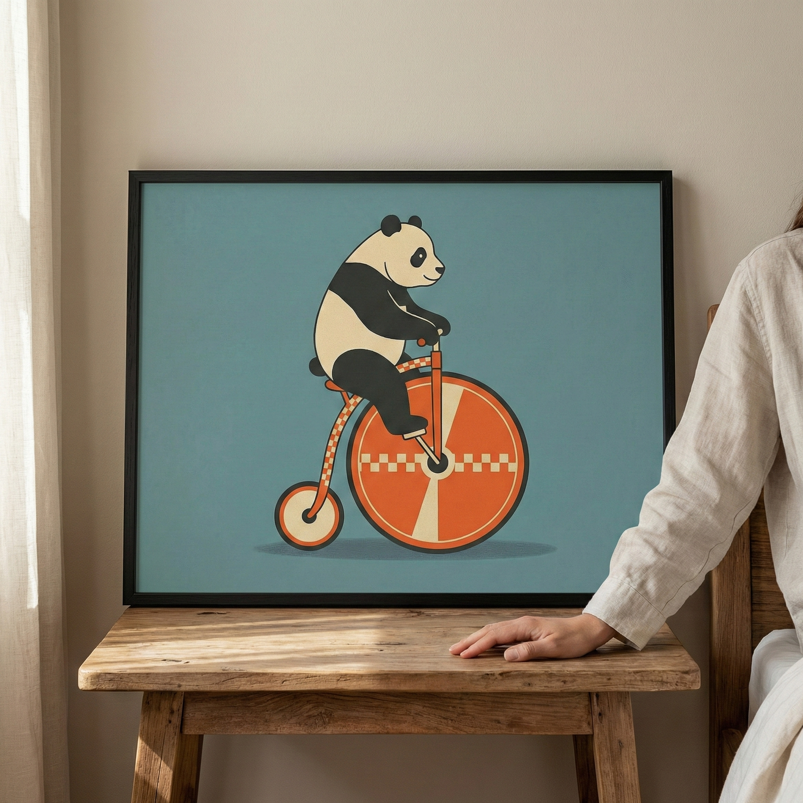 Framed panda animal on a bicycle wall art in a black frame, resting on a wooden table with a hand visible nearby.
