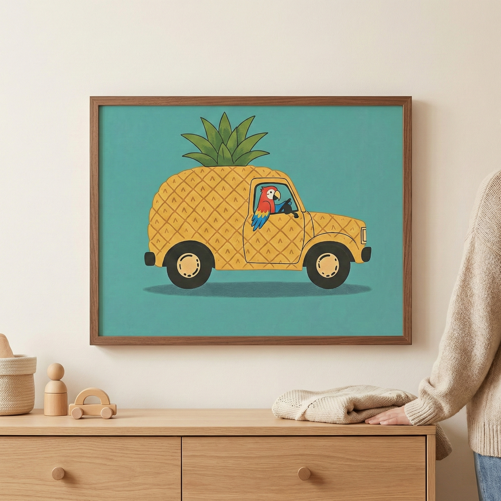 Framed pineapple car wall art featuring a bird driver, shown hanging in a brown wooden frame on a light-colored wall with a person's hand touching the bottom corner.