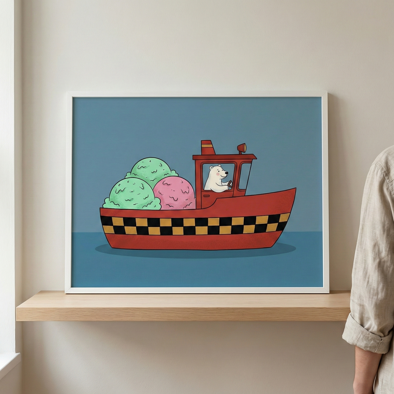 White framed polar bear driving a boat filled with ice cream wall art resting on a wooden shelf against a plain wall, with a person's shoulder visible on the right.