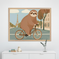 Modern kid's room with a white dresser. A large framed illustration of a smiling brown sloth riding a bicycle in Paris, with the Eiffel Tower, hangs centered above the dresser. A ceramic sloth, wooden blocks, and a eucalyptus sprig are on the dresser.