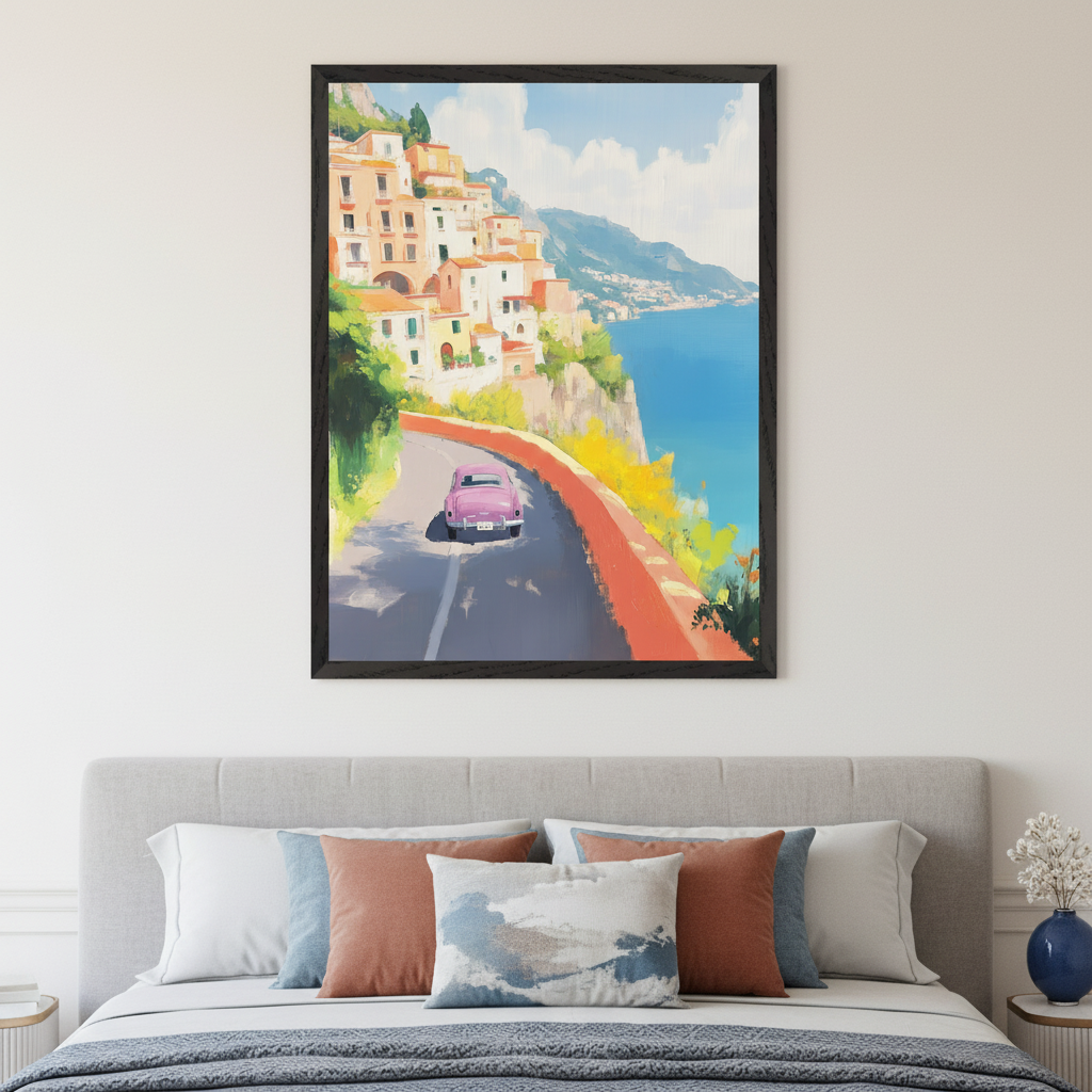 Modern bedroom with a light gray upholstered bed. A framed painting of a pink car on a coastal road with white and orange houses, green hills, and a blue ocean hangs centered above the bed. The art has a painterly style.
