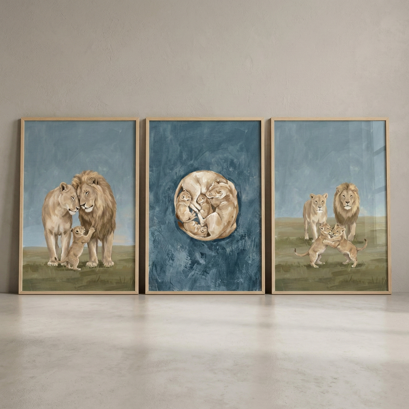 A triptych of three vertically framed illustrations featuring a lion family. On the left, a male lion and a lioness stand together as a small cub reaches up towards them. The center piece shows a lioness and her cubs curled into a circle against a textured dark blue background. The right illustration depicts two young cubs playing in the foreground with their parents standing behind them. All three scenes are rendered in a soft, illustrative style with light wood frames, displayed on a neutral wall.