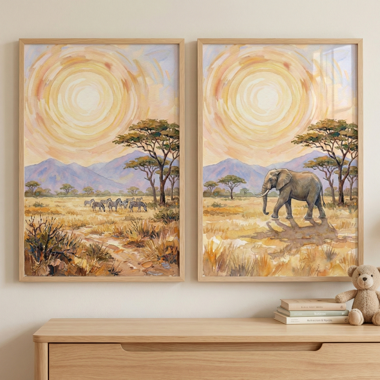 Two framed savanna-themed illustrations hang on a cream wall. Each artwork features a large, stylized sun of concentric warm circles above purple mountains and acacia trees. The left piece shows a herd of zebras in golden grasslands, while the right depicts a large elephant walking, casting a shadow. Housed in light wood frames, they sit above a wooden dresser. On the dresser is a stack of three books and a small plush bear. The style is soft and textured, using a warm watercolor aesthetic.
