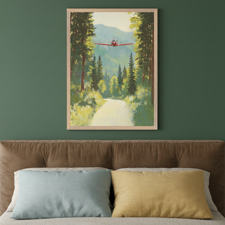 Contemporary bedroom with a dark green wall and a brown upholstered bed with light blue and yellow pillows. A framed painting hangs above the bed, depicting a red airplane flying over a forest road with tall green trees and mountains, in a naturalistic style.
