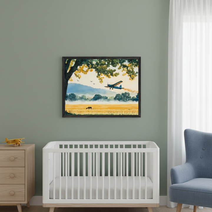 Modern nursery with a sage green wall. A white crib, wooden dresser, and blue armchair are visible. A framed watercolor painting of a crop duster plane spraying a golden field with a cow, misty hills, and a tree hangs centered above the crib.