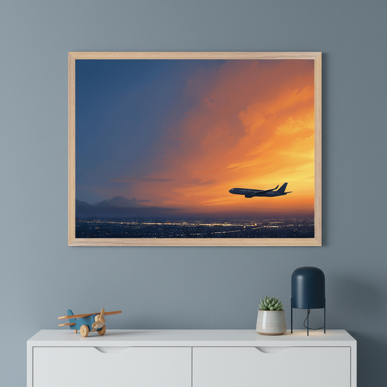 Framed artwork of a commercial airplane flying across a glowing sunset sky with vibrant orange and deep blue tones, displayed above a white dresser with a toy plane, succulent, and modern lamp.