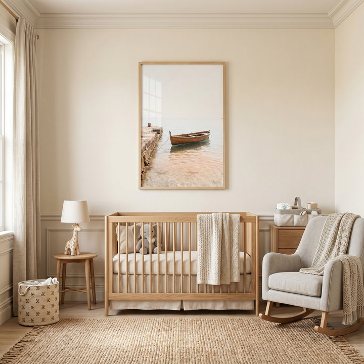 A neutral nursery with a wooden crib, rocking chair, and airy coastal wooden boat wall art in a light wood frame.