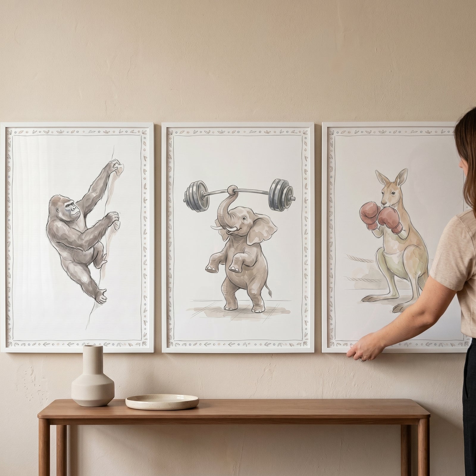 A person adjusts an antique sepia athletic animals wall art set of 3 featuring a gorilla, elephant, and kangaroo.