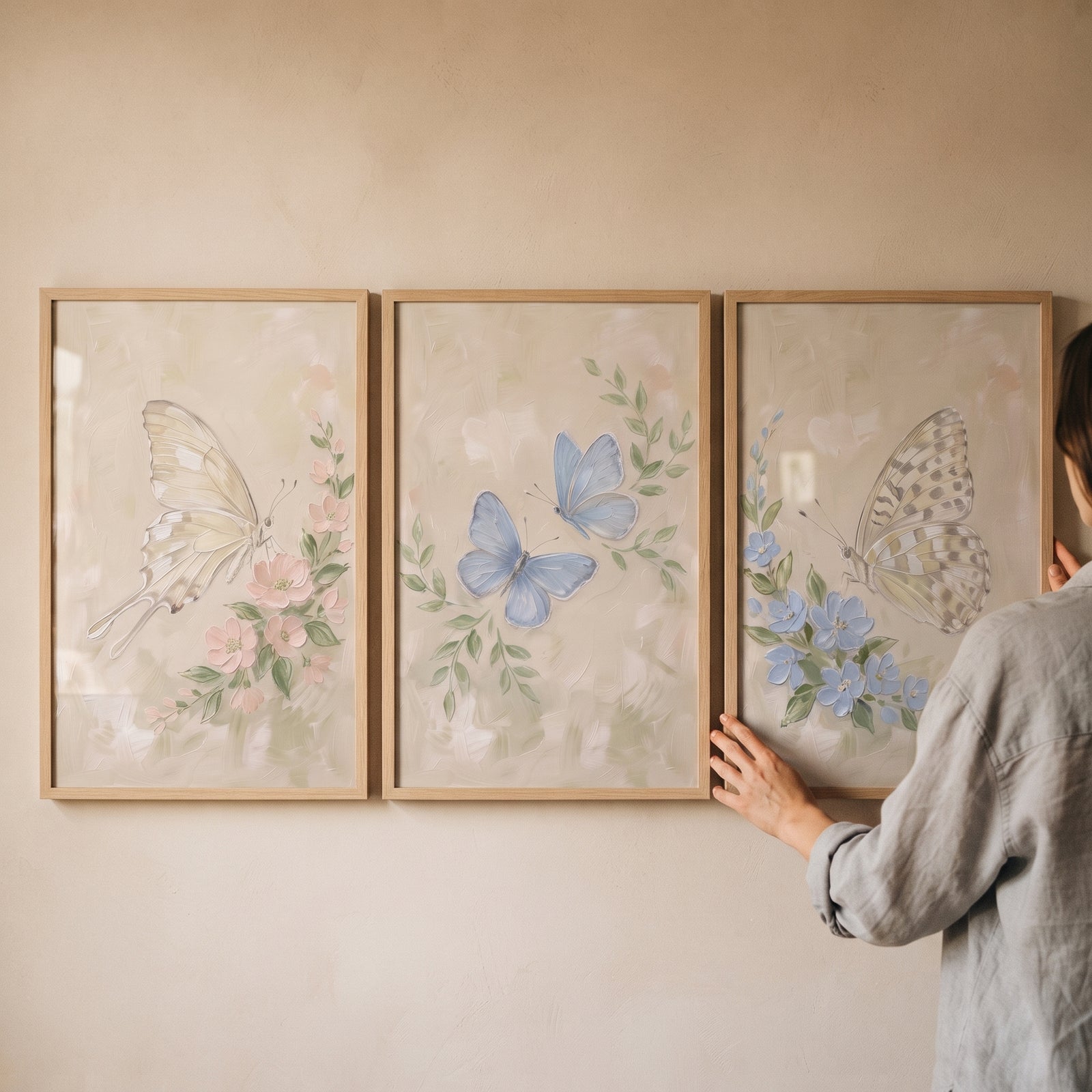 A person hangs an antique texture botanical butterfly wall art set of 3 in wooden frames on a beige wall.