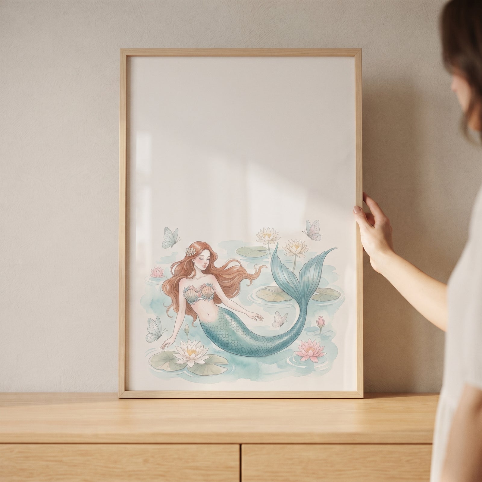Hand touches framed auburn hair aquatic mermaid wall art of a mermaid swimming among watercolor lilies and butterflies.
