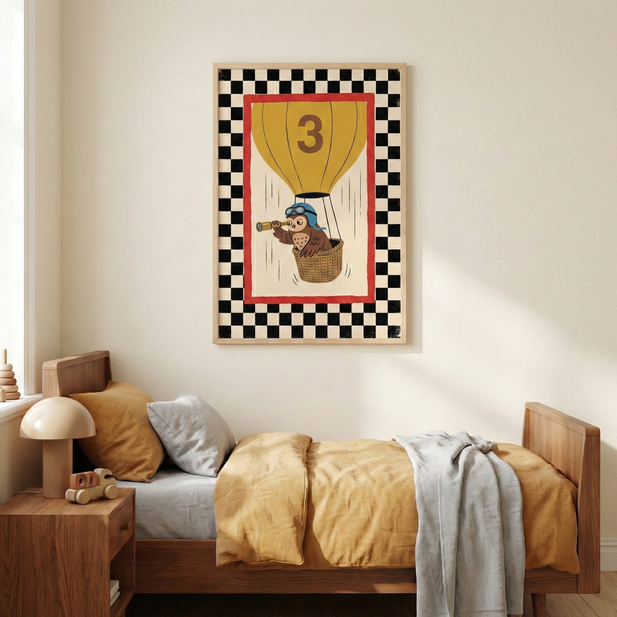 A cozy child's bedroom with a wooden bed dressed in mustard yellow and grey bedding. Hanging on the neutral-toned wall above the bed is a framed illustration of a cartoon owl in a yellow hot air balloon marked with the number three. The owl wears blue aviator goggles and looks through a telescope from the balloon's basket. The artwork features a red inner frame and a black and white checkered border. To the left of the bed, a wooden nightstand holds a beige mushroom-shaped lamp and a small wooden toy truck.