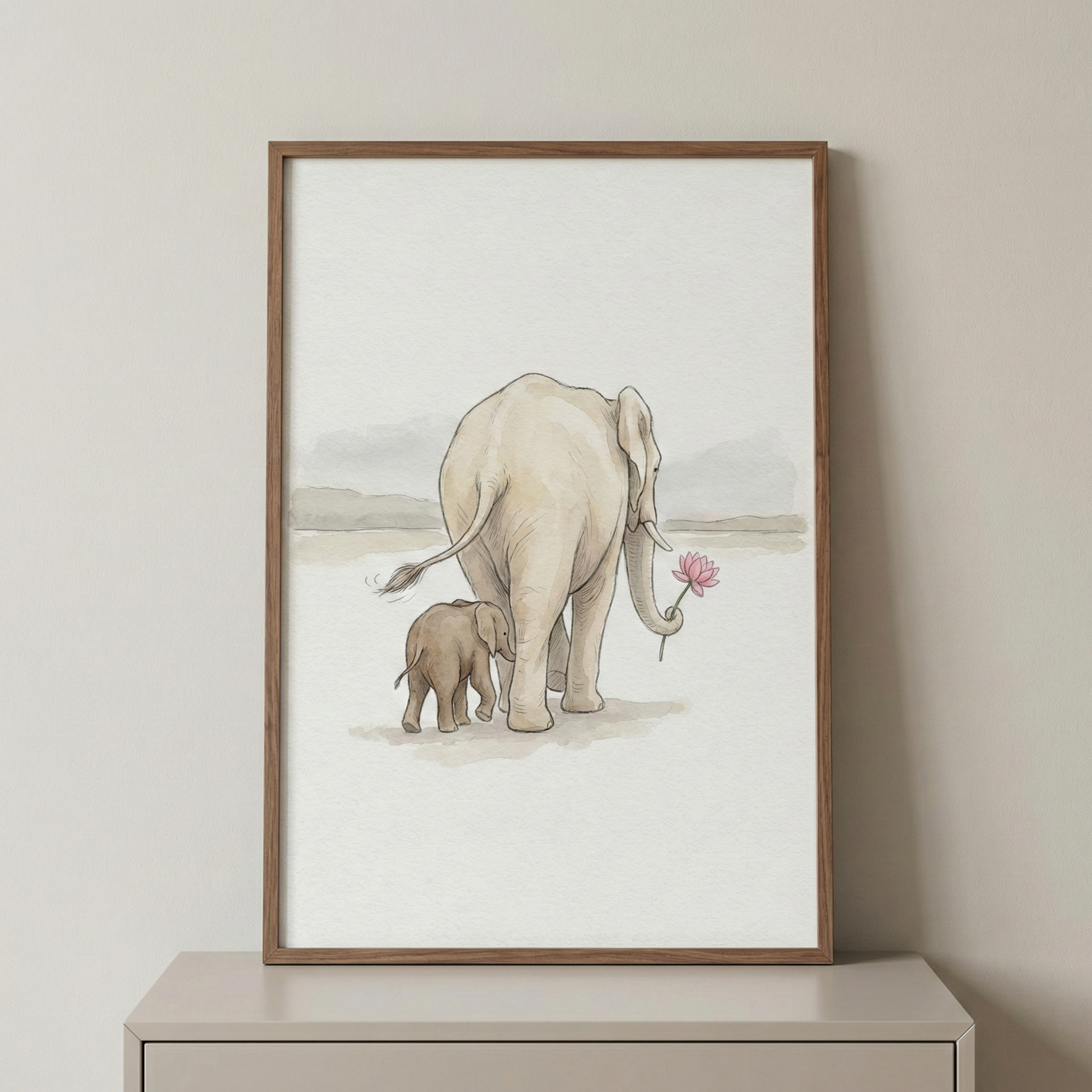 A vertical framed piece displays a minimalist watercolor-style illustration of an adult elephant and its calf walking away. The larger elephant, colored in soft cream, holds a pink flower in its trunk. Beside it, the smaller calf is a darker shade of gray. They travel across a light, hazy landscape. The artwork is set in a thin, natural wood frame and sits on a neutral surface against a plain wall.