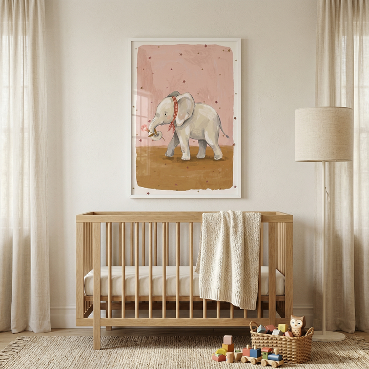 A serene nursery setting features a light-toned wooden crib centered against a warm, neutral wall. A thick, cream-colored knitted blanket is draped over the crib's side. Hanging above is a framed piece of artwork depicting a friendly gray elephant with a red checkered scarf, walking across a brown surface under a soft pink sky filled with tiny stars. 