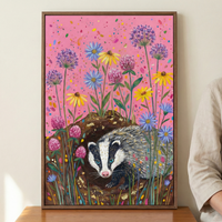 A whimsical artwork in a wooden frame depicts a badger with bright blue eyes peeking from a dark burrow. The ground around the hole is textured with gold accents. Tall, stylized flowers in shades of purple, yellow, blue, and pink rise up against a vibrant pink background. The sky is filled with colorful, confetti-like speckles. The badger's fur is detailed with white, black, and grey strokes. The overall style is colorful and folk-inspired.