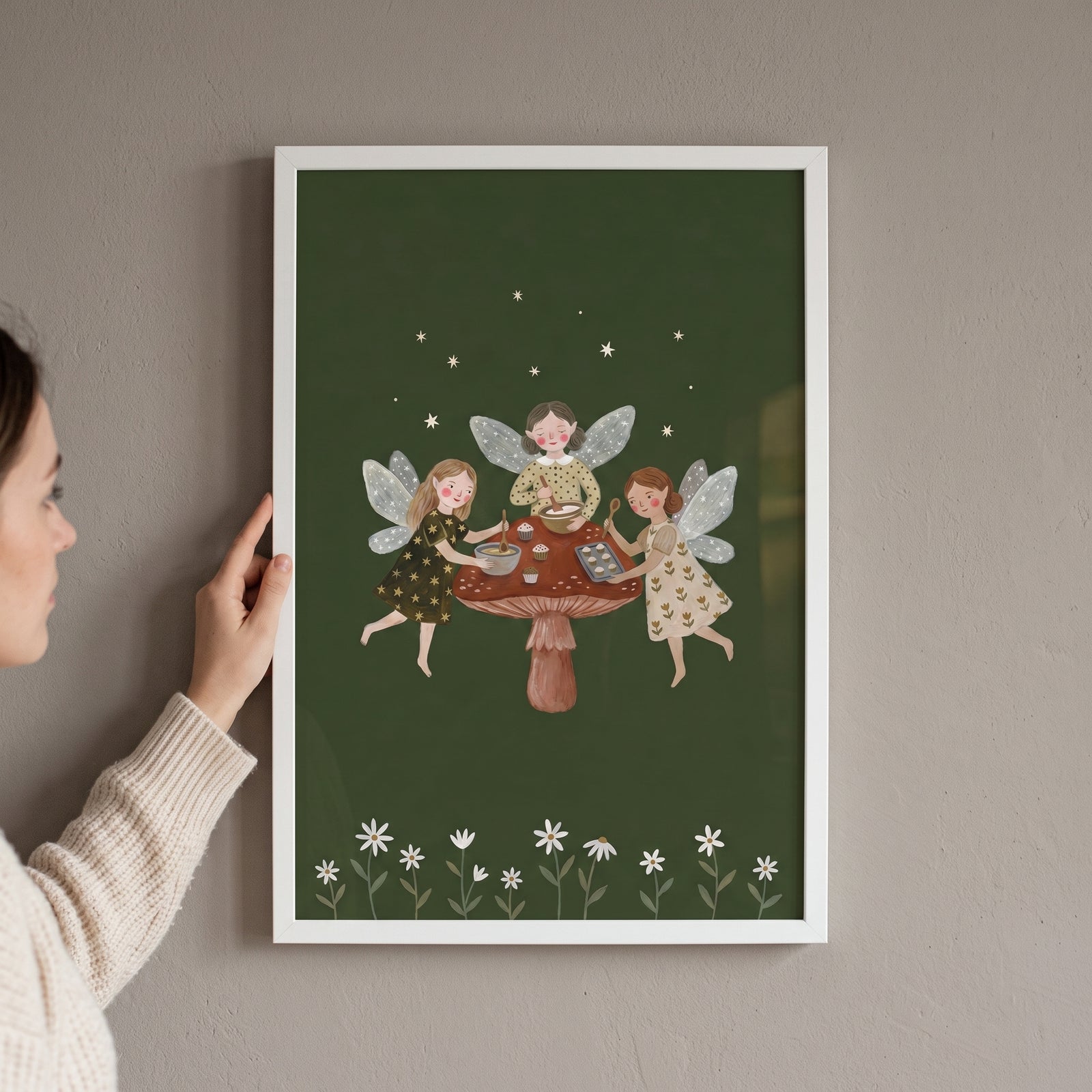 A woman holds a framed baking mushroom garden fairies wall art print showing fairies baking on a large mushroom cap.