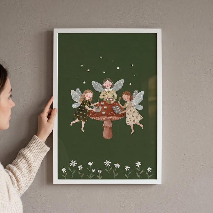 A woman holds a framed baking mushroom garden fairies wall art print showing fairies baking on a large mushroom cap.