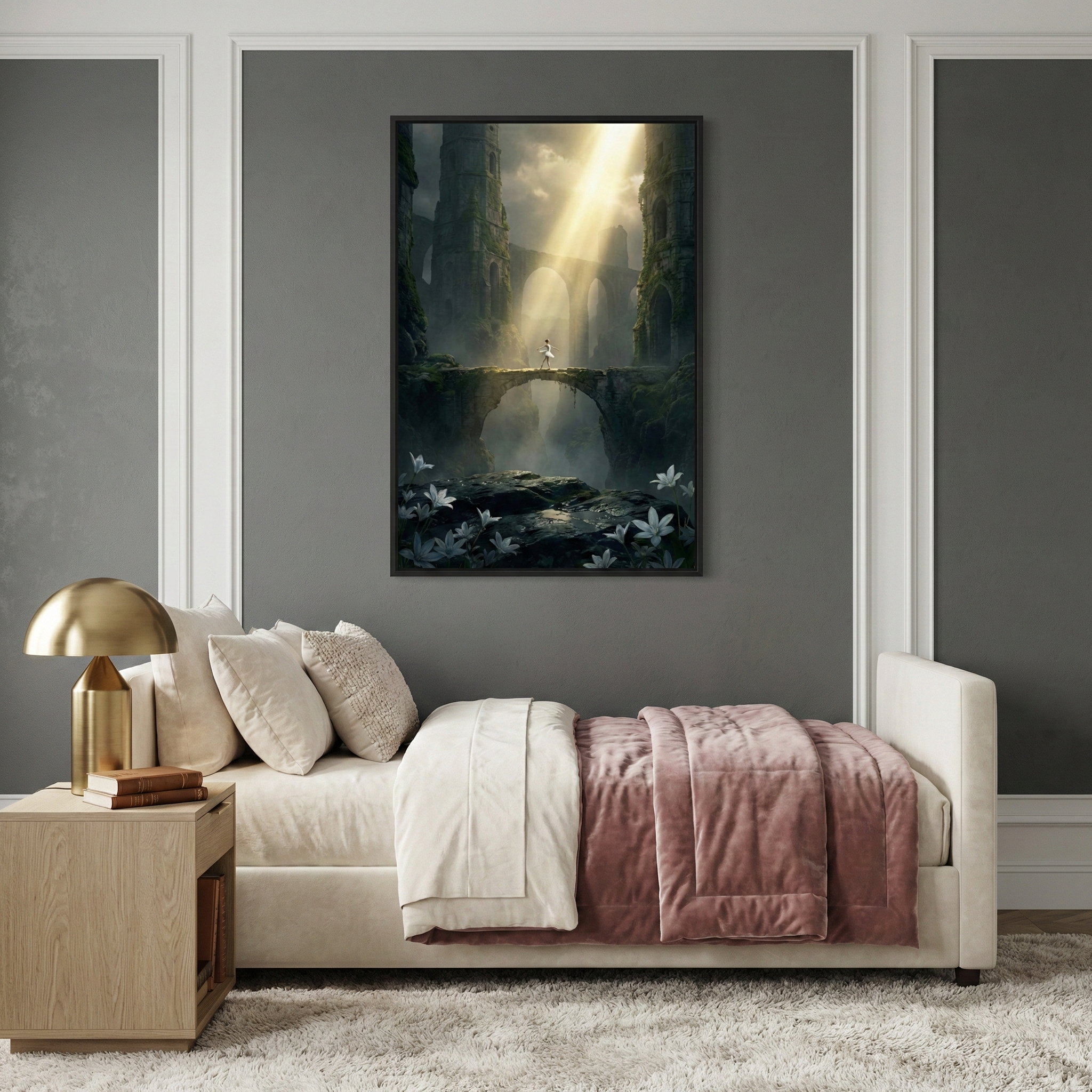 A vertical framed artwork hangs on a dark gray wall above a light-colored daybed. The artwork features a fantasy scene where a small white-clad figure stands on a high stone bridge between two massive mossy stone towers, illuminated by a singular beam of light from above. White lilies bloom in the dark shadows below. The daybed is topped with several pillows and a dusty rose throw blanket. A light wood nightstand to the left holds a gold dome lamp. The room has decorative white wall molding.