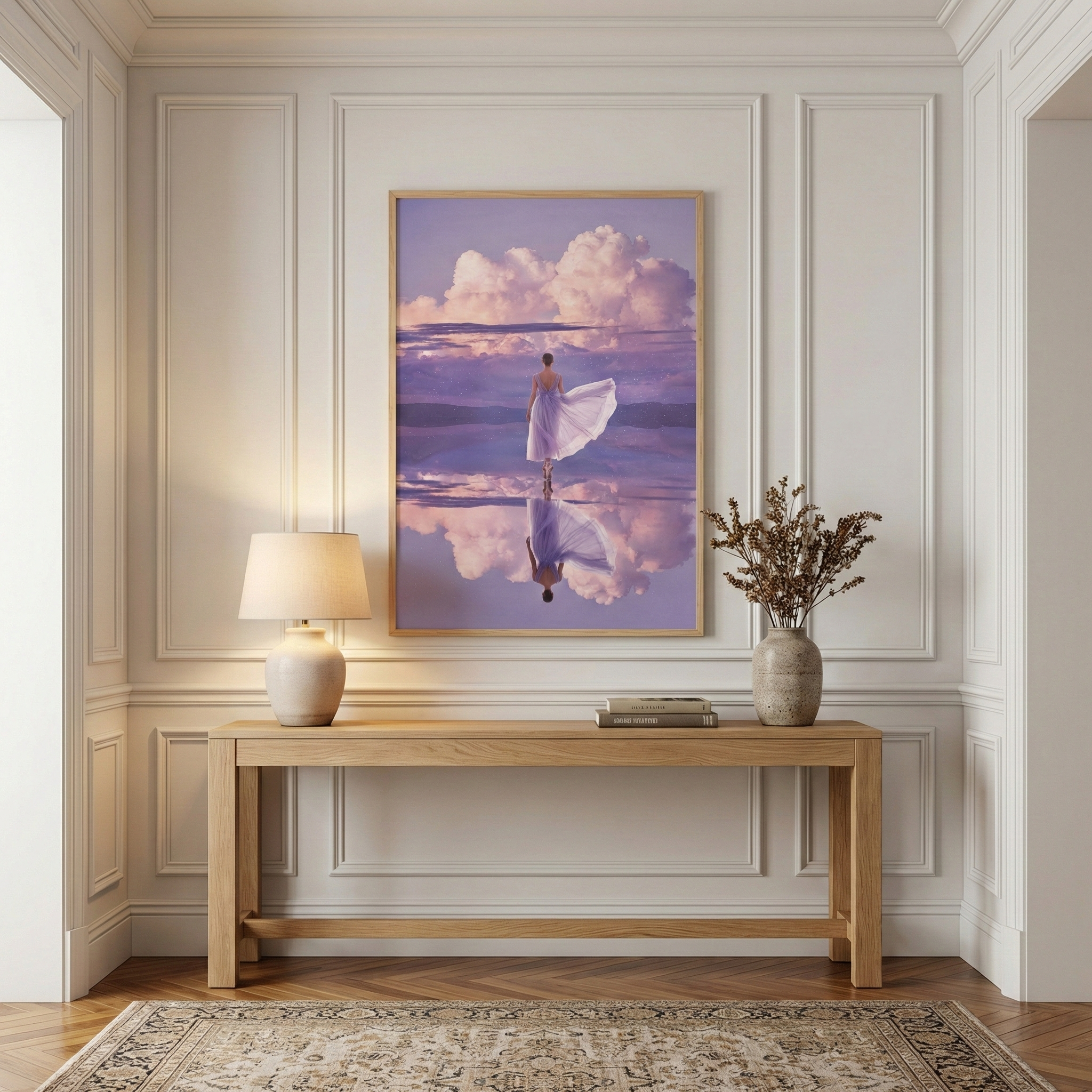A large vertical framed print is the central focus of a refined interior space, mounted on a cream-colored wall adorned with elegant rectangular picture frame moldings. The print depicts a serene and ethereal scene where a figure in a light, flowing lavender-hued dress walks across a mirror-like expanse of water.