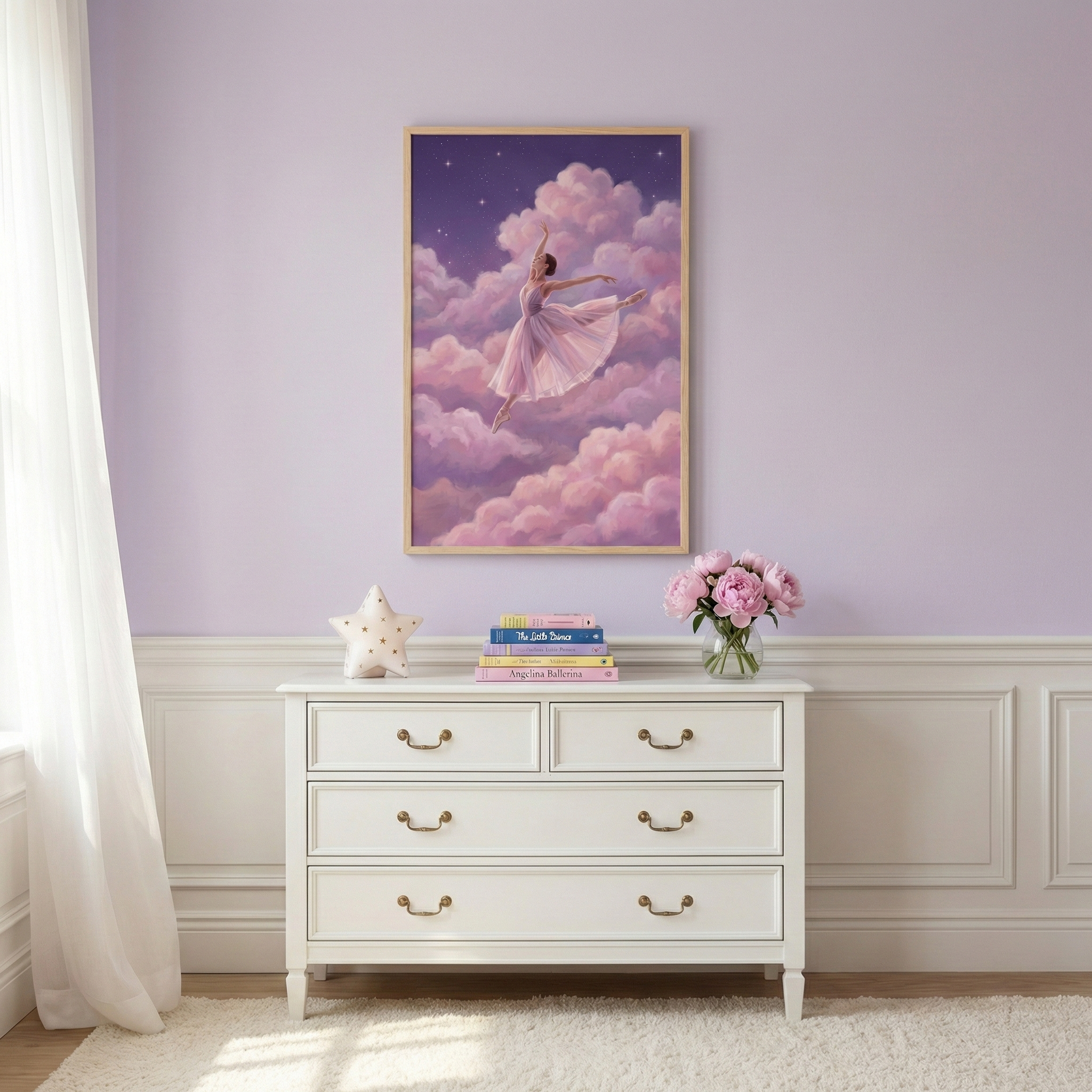 A serene room features a framed piece of art on a light purple wall, depicting a dancer in a pink tutu leaping through soft, fluffy pink and purple clouds under a starry night sky. Below the art, a white dresser with gold handles holds a stack of colorful children's books, a white star-shaped decorative object, and a glass vase filled with pink flowers. A sheer white curtain hangs to the left, and the bottom half of the wall is decorated with white wainscoting above a plush white rug.