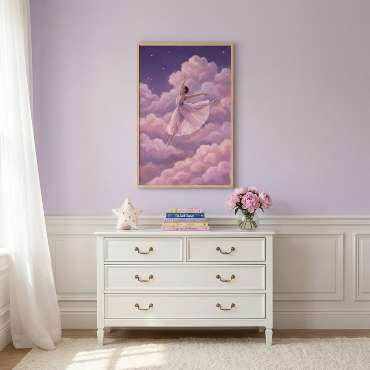 A serene room features a framed piece of art on a light purple wall, depicting a dancer in a pink tutu leaping through soft, fluffy pink and purple clouds under a starry night sky. Below the art, a white dresser with gold handles holds a stack of colorful children's books, a white star-shaped decorative object, and a glass vase filled with pink flowers. A sheer white curtain hangs to the left, and the bottom half of the wall is decorated with white wainscoting above a plush white rug.