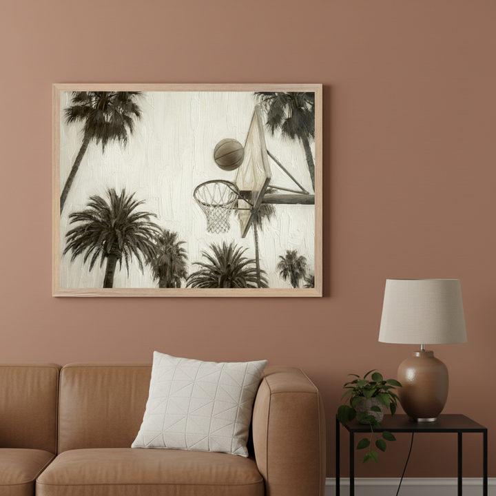 Living room with a brown leather sofa. A large framed sepia-toned, textured painting of a basketball entering a hoop amidst palm trees hangs above the sofa. A black side table with a brown lamp and a plant sits to the right of the sofa.