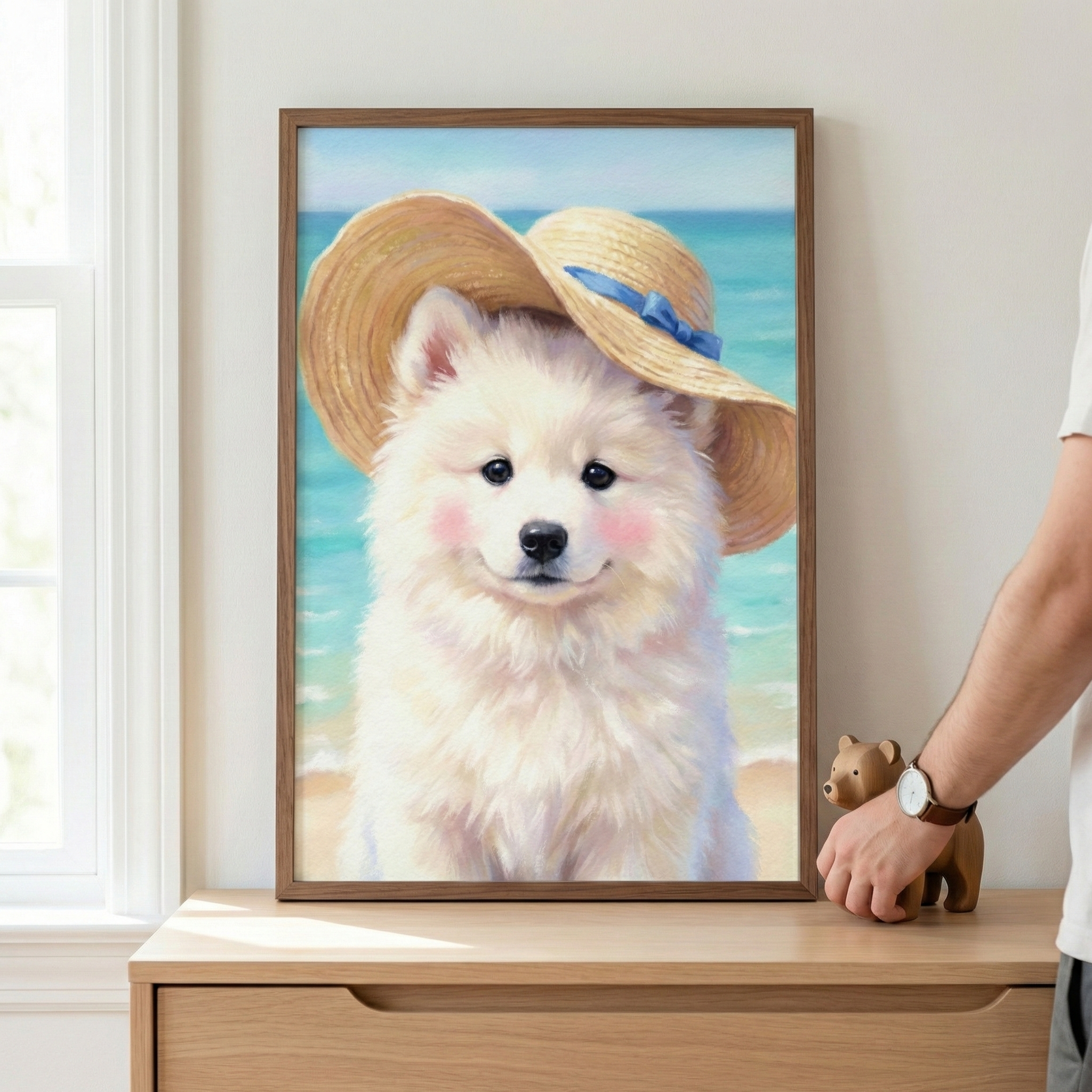 A person adjusts a framed painting of a fluffy white dog wearing a straw hat with a blue ribbon, set against a beach backdrop. The painting rests on a wooden dresser, with a small bear figurine beside it.