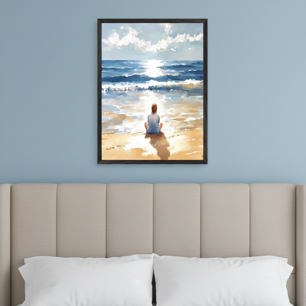 Bedroom with a beige upholstered headboard and white pillows. A framed painting depicting a person sitting on a sunny beach gazing at the ocean hangs centrally on a blue wall above the bed. The artwork shows waves, clouds, and sun glare on the water.