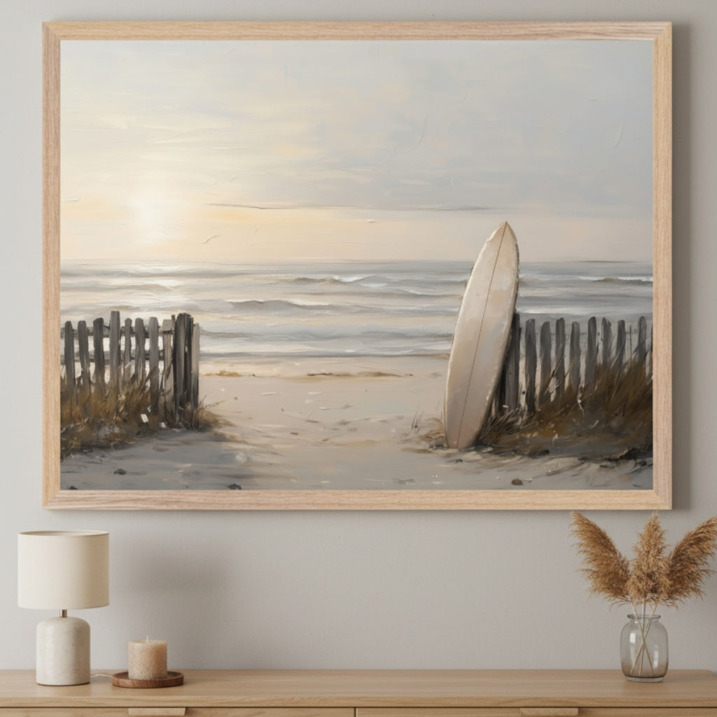 Modern living room with a light wood dresser. A large framed impressionistic painting of a beach path leading to the ocean at sunset, with a surfboard leaning against a wooden fence, hangs centered above the dresser. A lamp and candle are on the left, dried grass in a vase on the right.